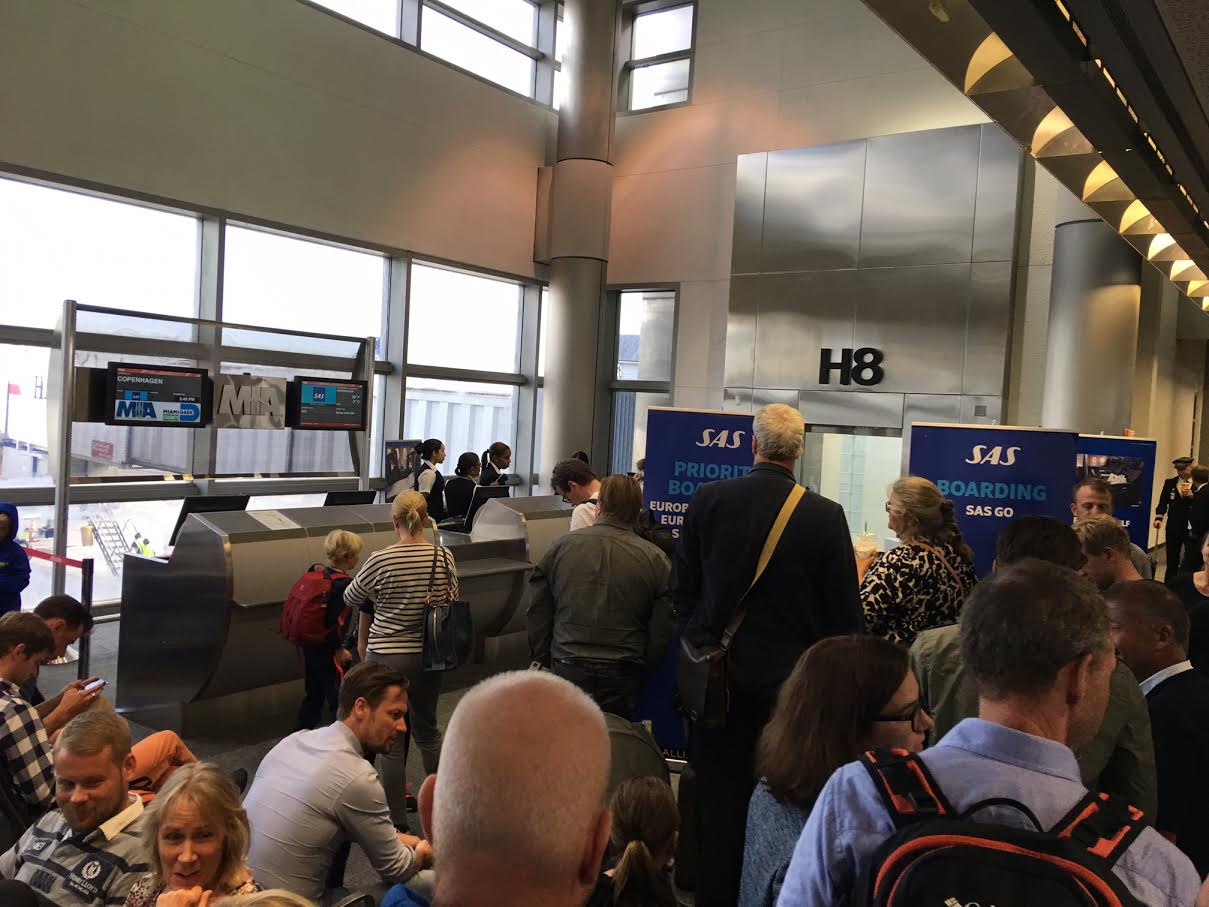 Kø ved gaten da passagererne venter i en time på en forsinket afgang. En forsinkelse, som var skabt af lufthavnen da det indkommende fly måtte vente en time for at komme til en gate.